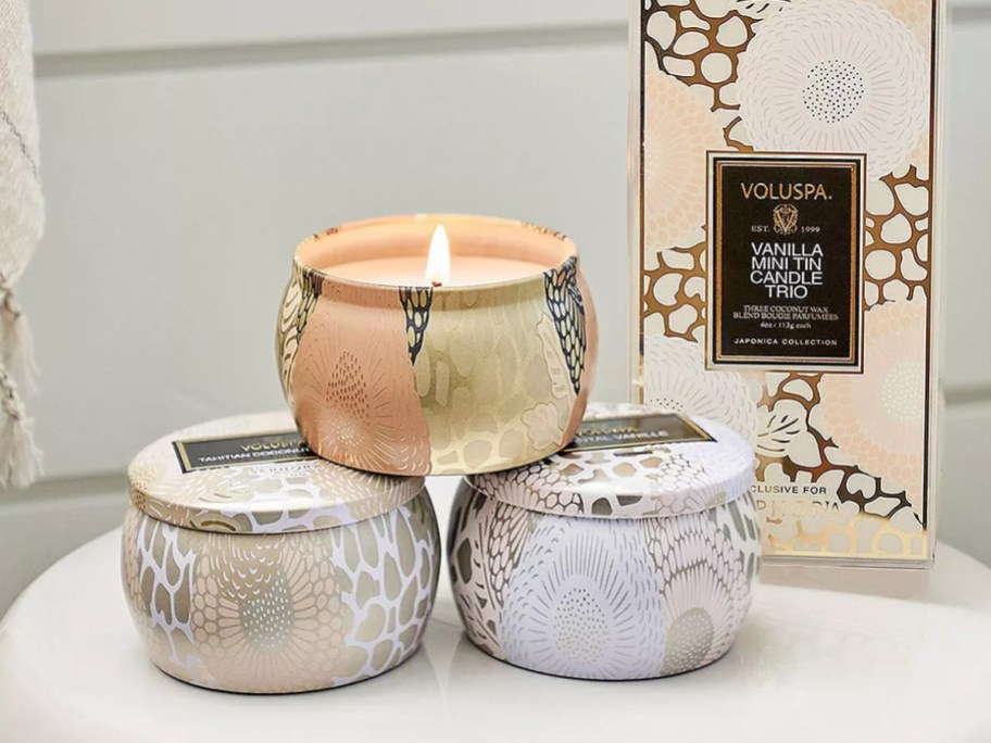 neutral color candle tins stacked, 1 lit, box they come in behind them
