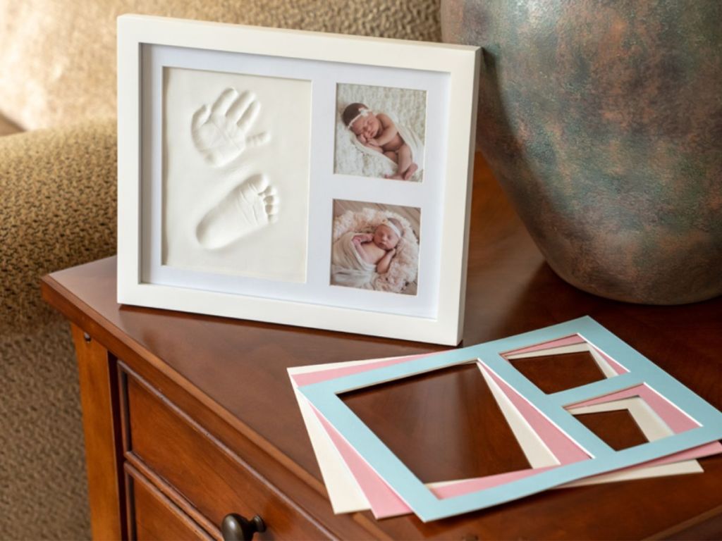 Baby Handprint & Footprint Kit w/ Photo Frame in White shown sitting on side table with different color mats