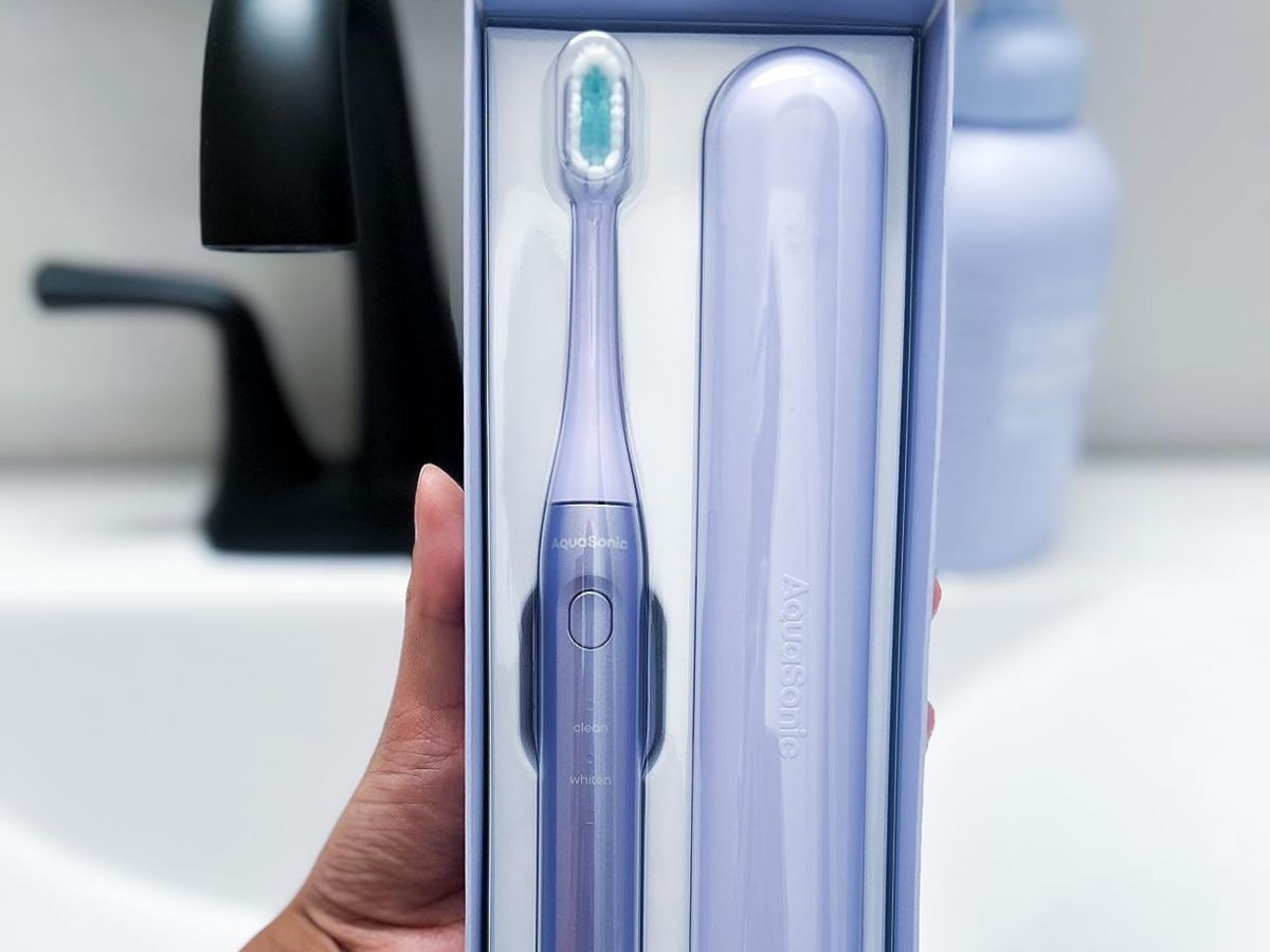 hand holding up package containing purple electric toothbrush and holder