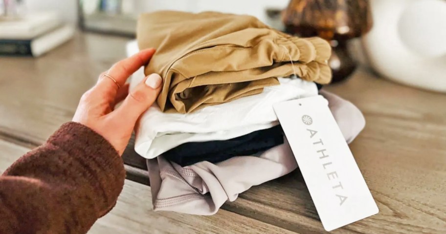 hand touching a stack of folded Athleta clothing