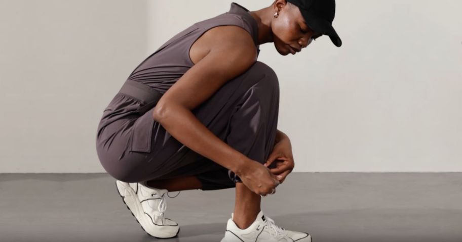 Woman bending over tying her shoe while wearing an Athleta jumpsuit