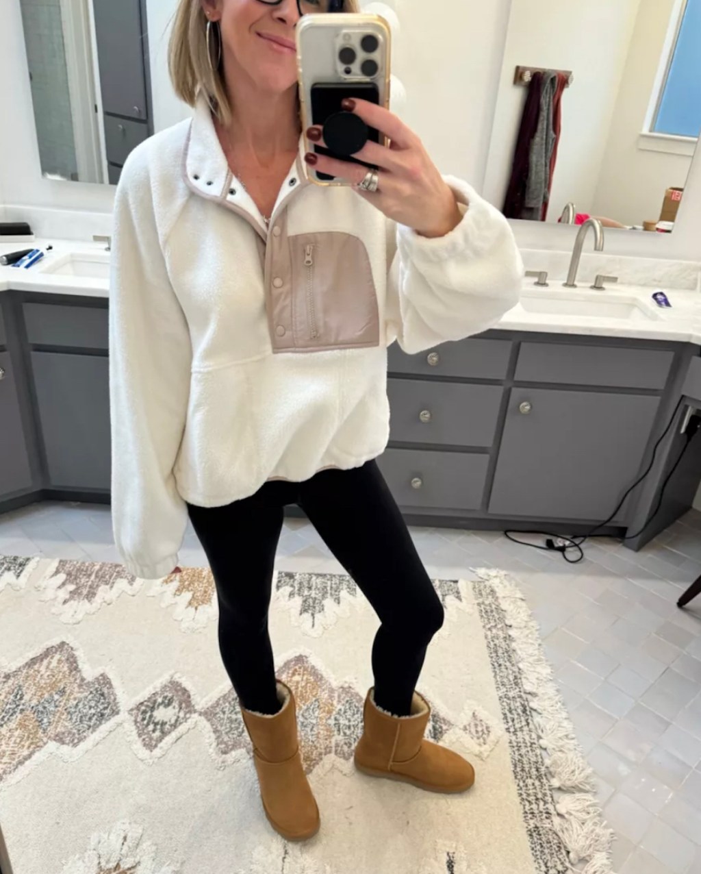 woman taking selfie in mirror wearing white pullover sherpa and black leggings with uggs