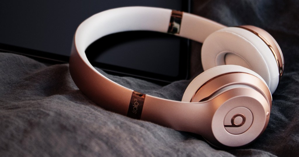 pair of rose gold Beats Solo 3 Wireless Headphones laying on bed