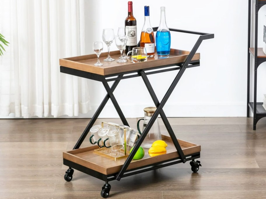black metal bar cart with wooden trays with bottles and glassware on top