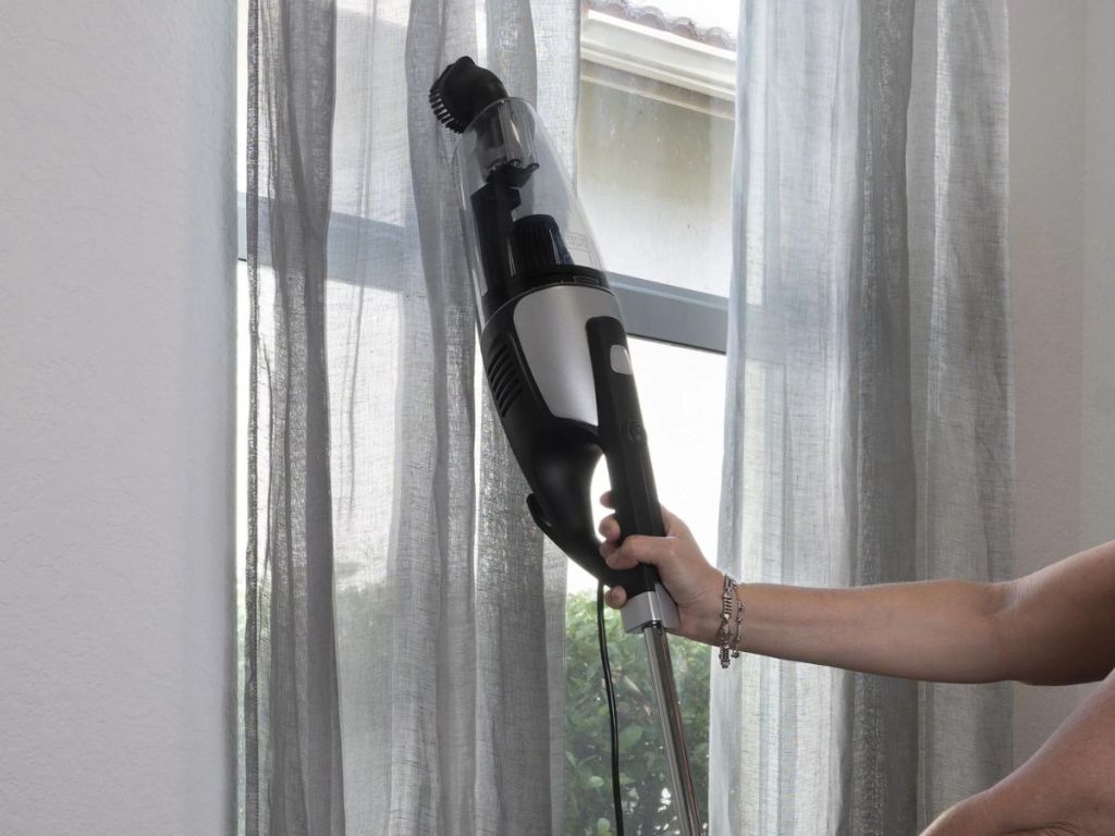 person cleaning curtains with handheld vacuum