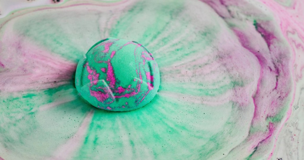 green and purple lush bath bomb in bathtub