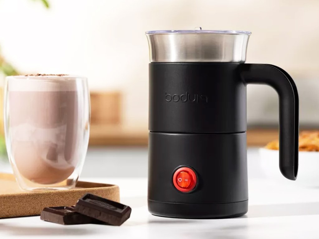 black milk frother next to cup of coffee