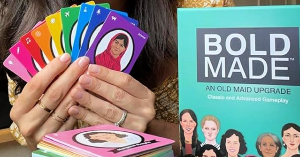 Person holding playing cards in their hand next to the bold made card game box