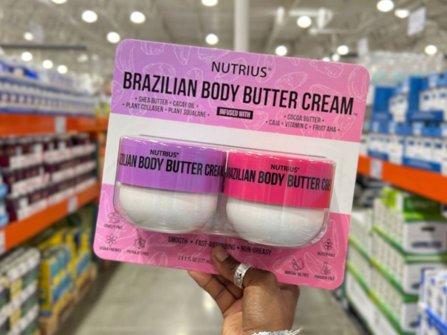 a womans hand holding a blister pack of two jars of body butter