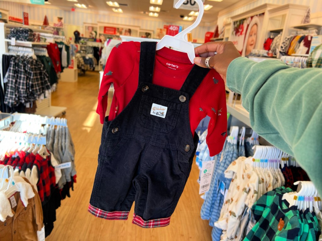 woman holding up holiday overall outfit inside carters store