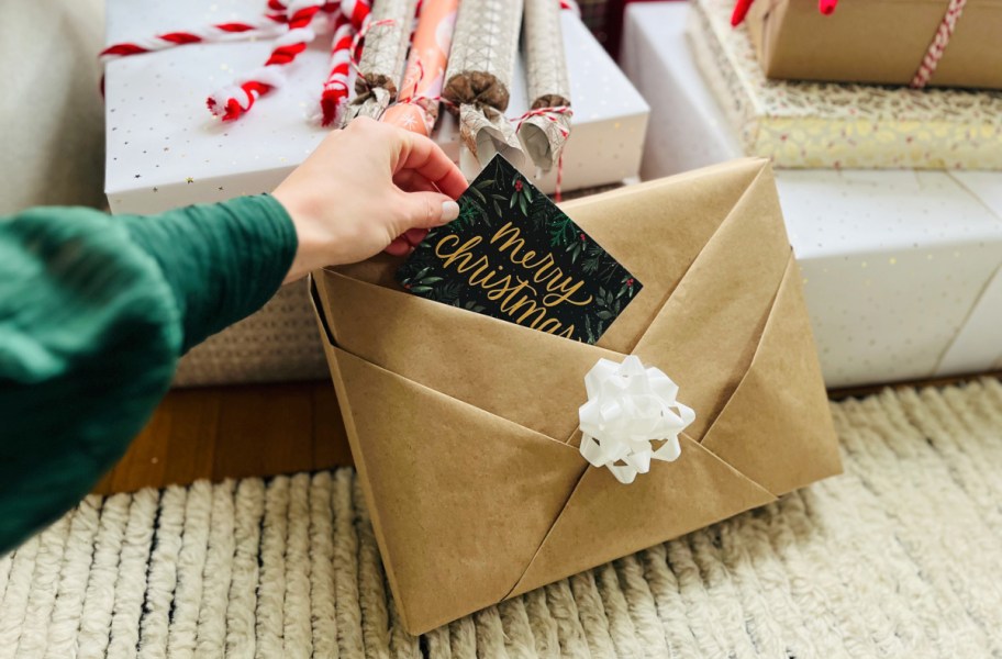 Hand placing a gift card into a wrapped christmas package