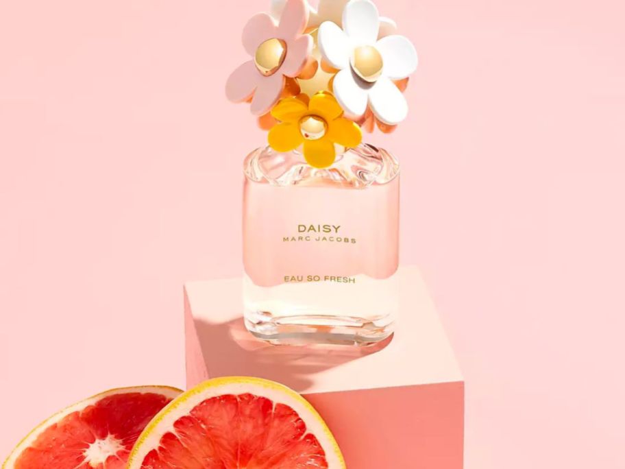 a bottle of Daisy eau so fresh by marc jacobs on a small pedestal next to a grapefruit half