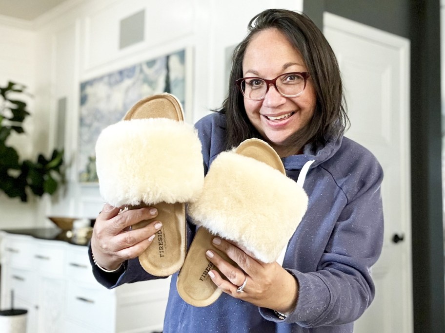 woman holding up a pair of fluffy white slipper slides