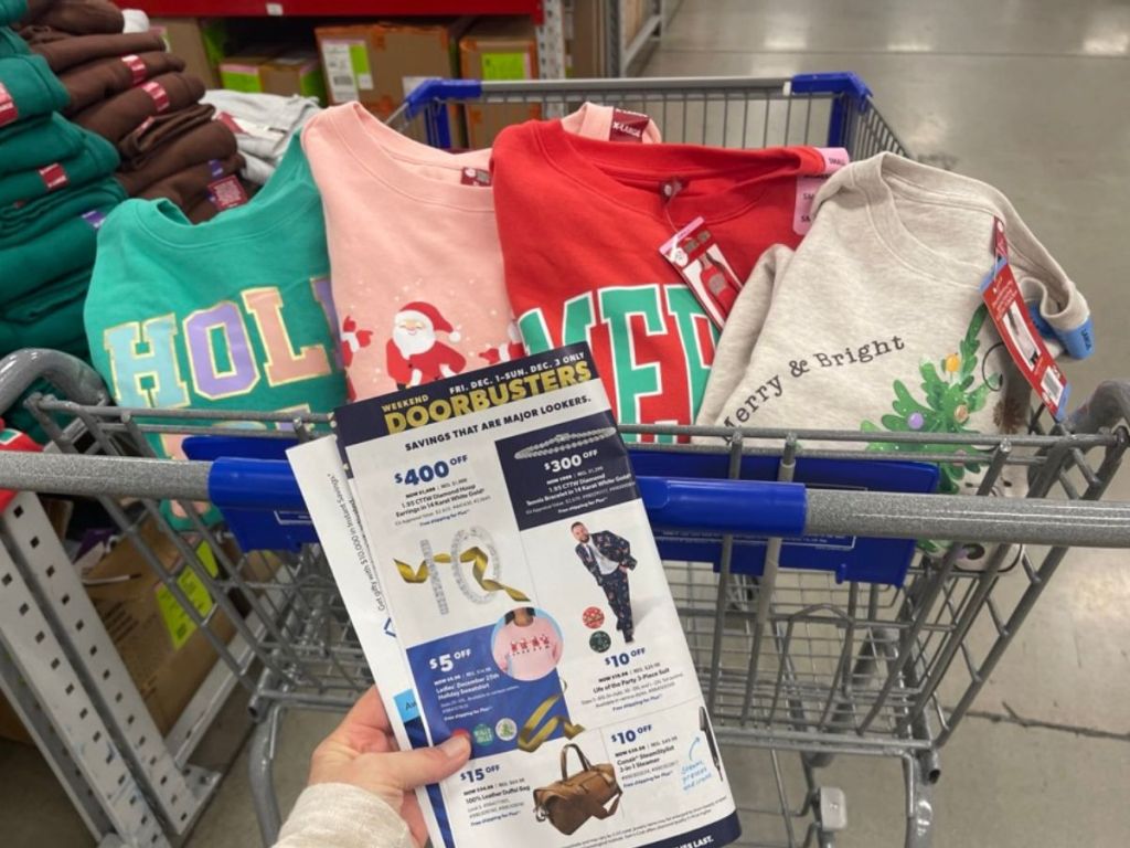 4 Dec. 25th Ladies Holiday Sweatshirts in a cart next to a womans hand holding a sale paper