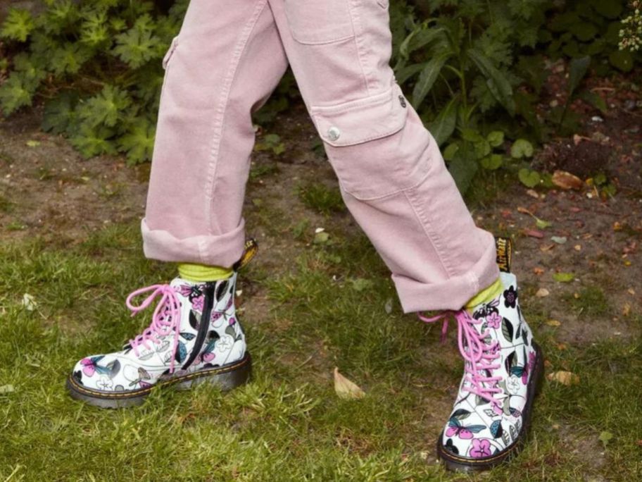 Child's legs and feet in the grass wearing a pair of Dr. Marten's graphic Meadow Print boots