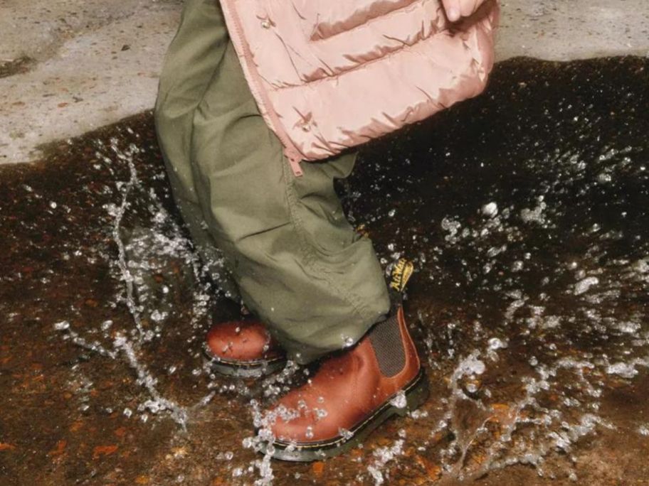 Child splashing in a puddle of water while wearing a pair of brown, fur lined Dr. Martens boots