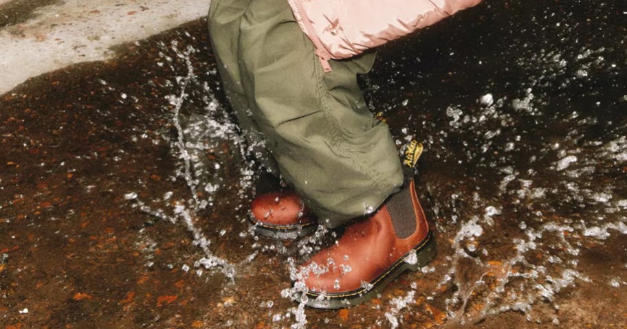 kid splashing in puddle in brown boots and green pants