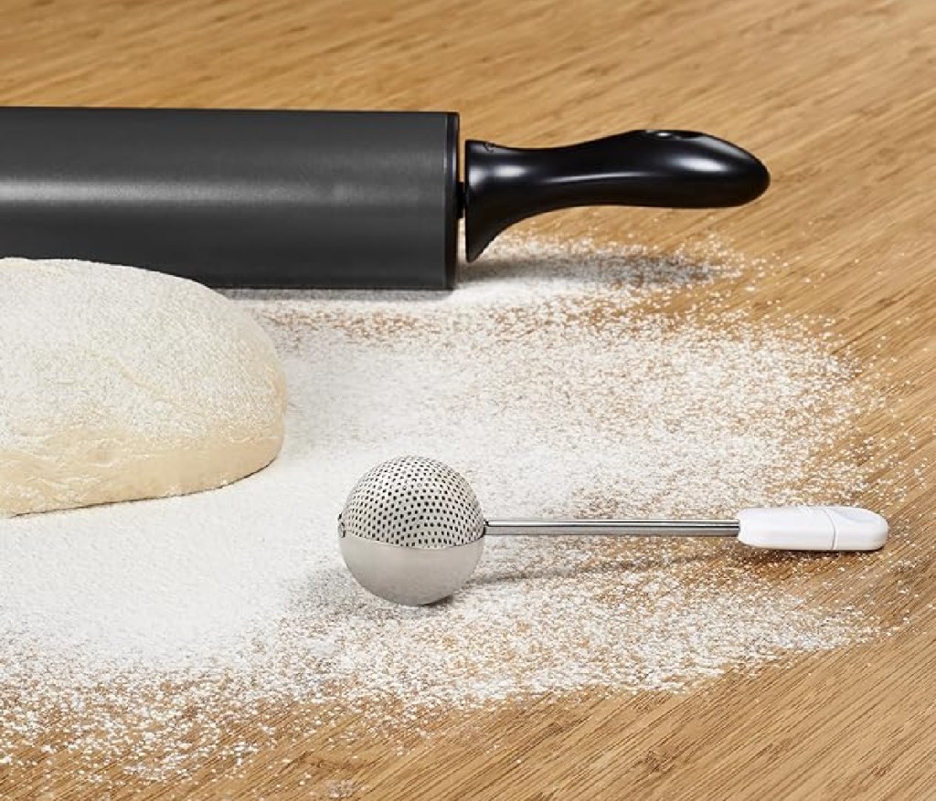 The OXO Good Grips Baker's Dusting Wand next to a dough and a rolling pin