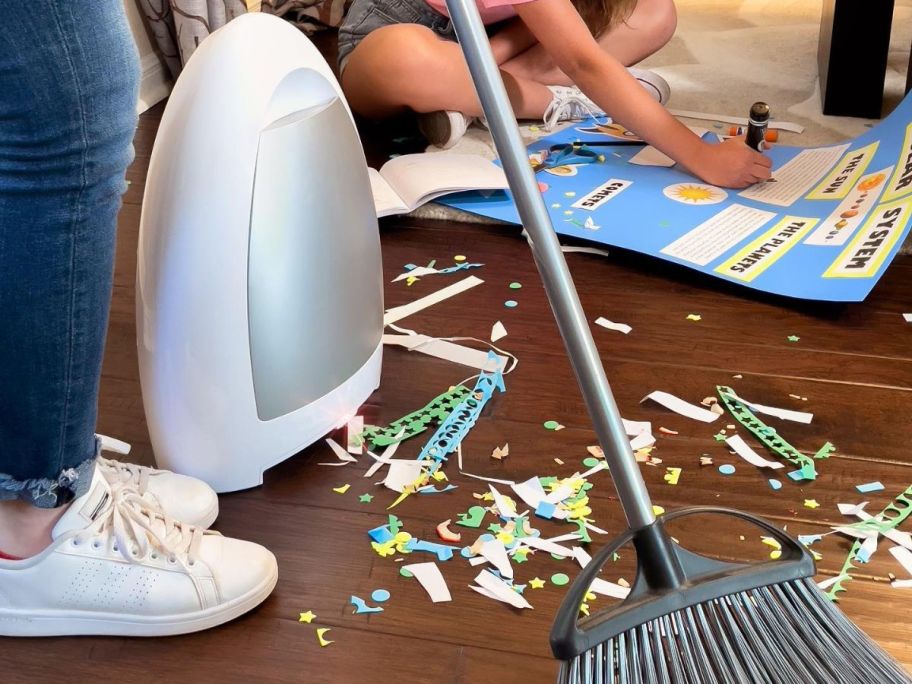 Person sweeping paper trimmings into an EyeVac while a child sits in the background making a poster