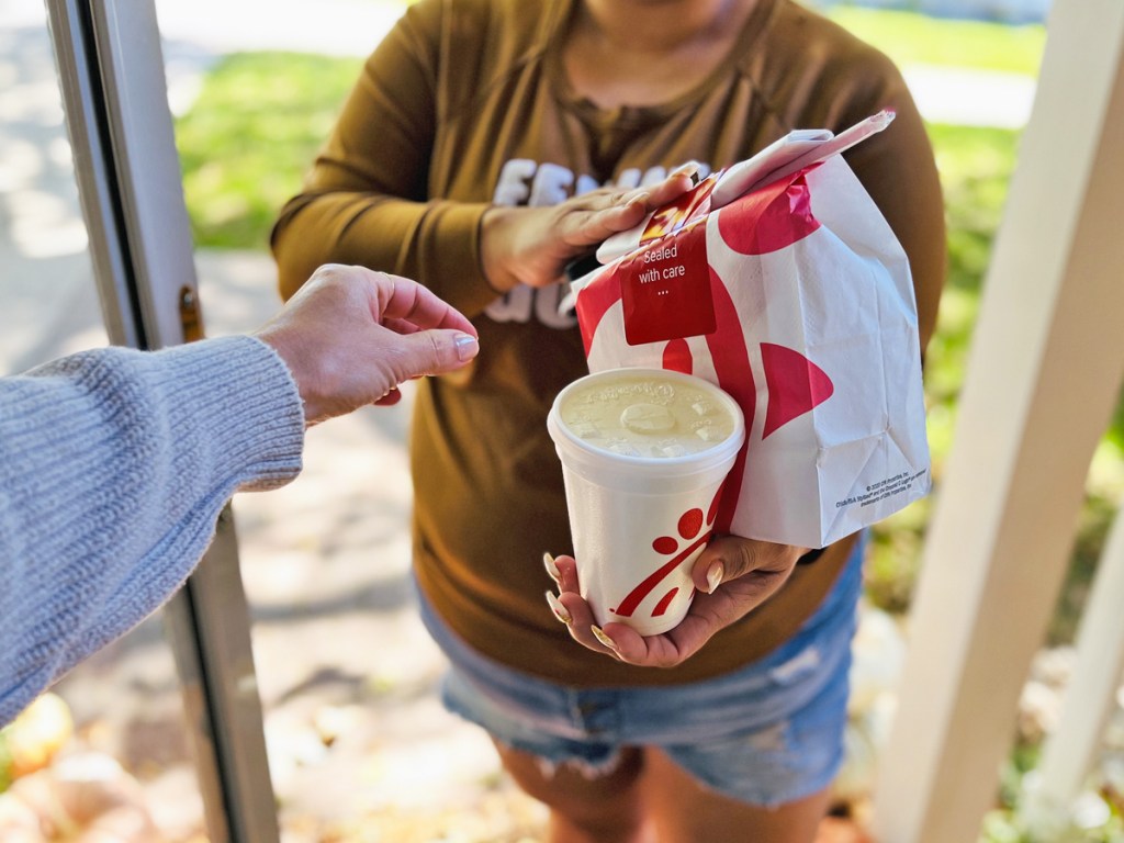 hand reaching out to take Chic-Fil-A bag and drink from delivery driver