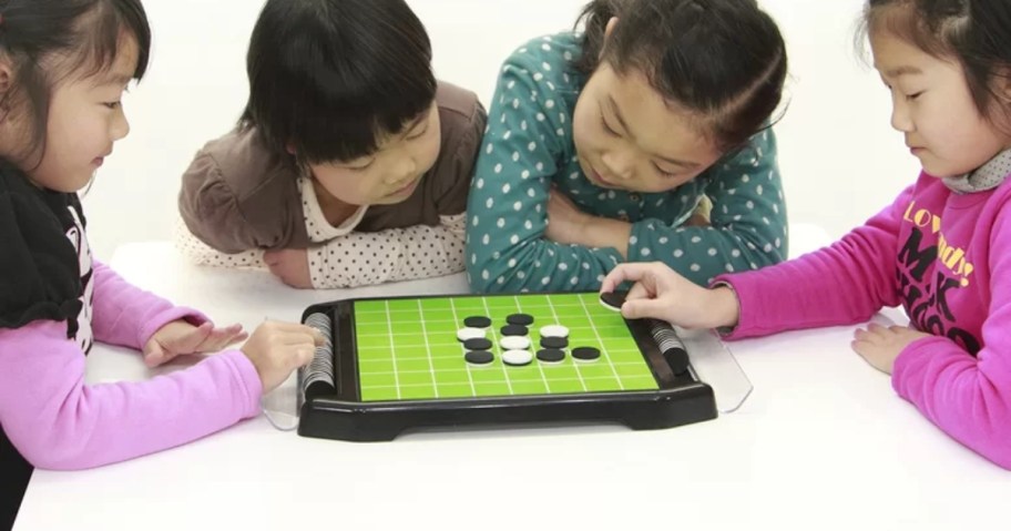 kids playing with a Go Game that has a green board and black and white round playing pieces