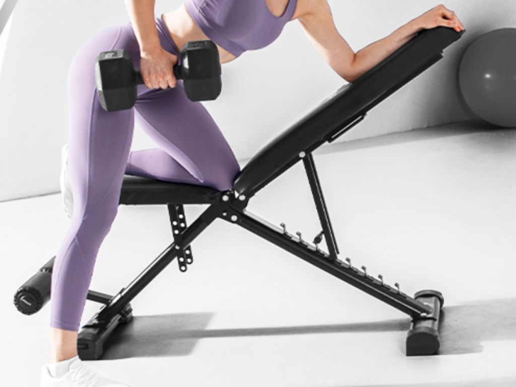 woman wearing purple workout clothes and holding a weight and working out on a Thramono Adjustable Weight Bench
