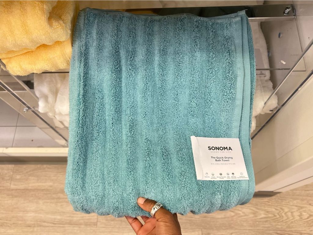 hand pulling a turquoise blue ribbed bath towel off a shelf
