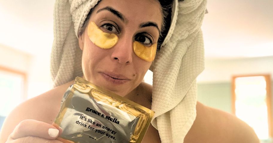 woman with towel on her head, wearing gold Grace & Stella under eye patches and holding up the packaging they came in