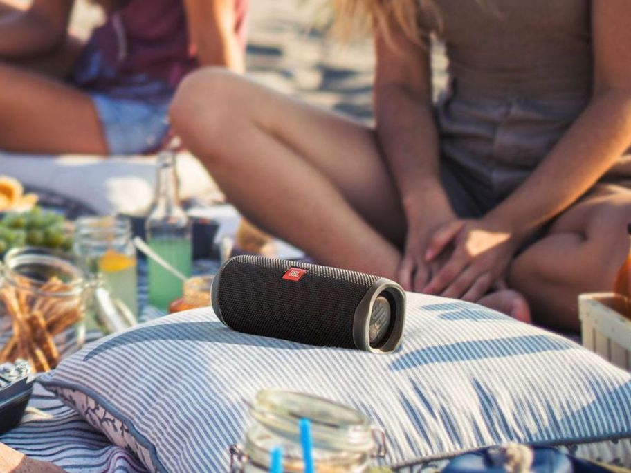 A pillow with a JBL speaker on it surrounded by teens at the beach