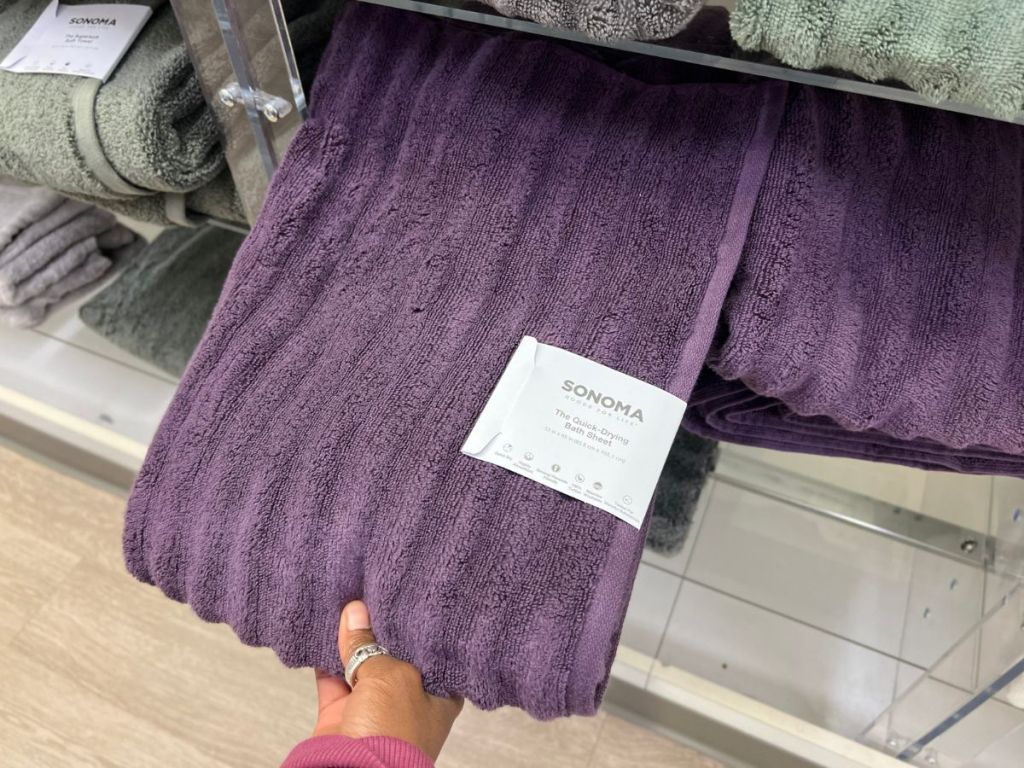 hand pulling a purple ribbed bath towel off a shelf