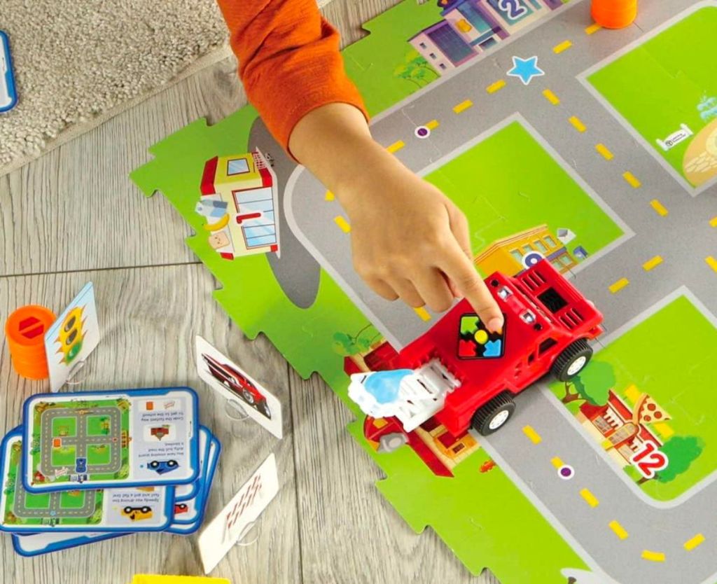 a little kid's hand pushing a button on the top of a toy truck included in the Learning Resources Switcheroo Coding Crew - 46 Pieces