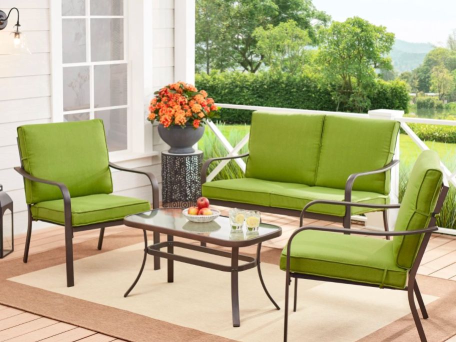 a love seat and two chairs with green coushions set up around a small square cocktail table