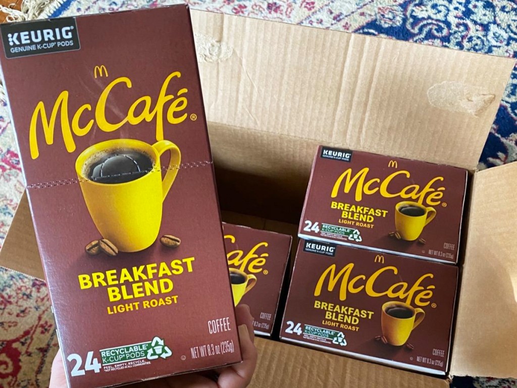 hand holding box of McCafe k-cups with box of more boxes in background