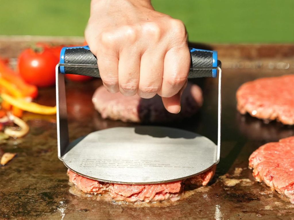 Hand using a Mr BBQ burger press to press down a patty on a griddle