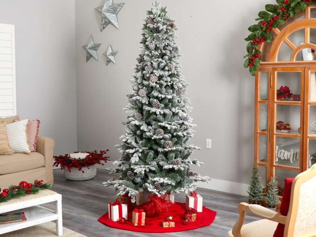 Tall and skinny flocked Christmas tree in living room with red tree skirt