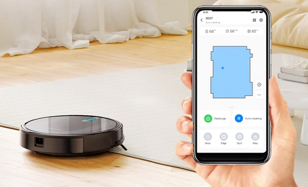 hand holding phone showing robot vacuum settings with vacuum in background