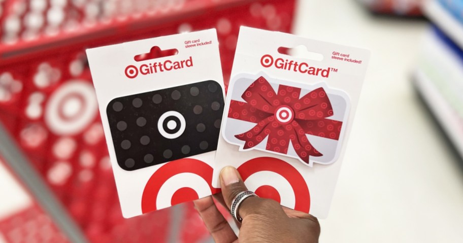 hand holding up two target gift cards in front of red shopping cart