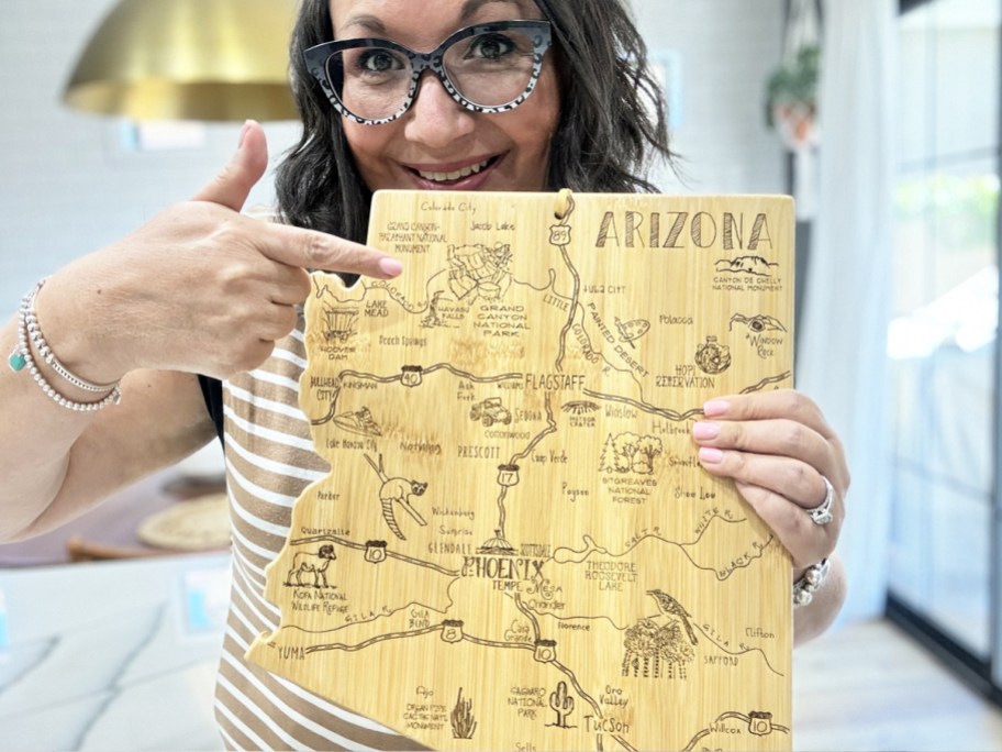 woman holding up and pointing to an arizona shaped cutting board