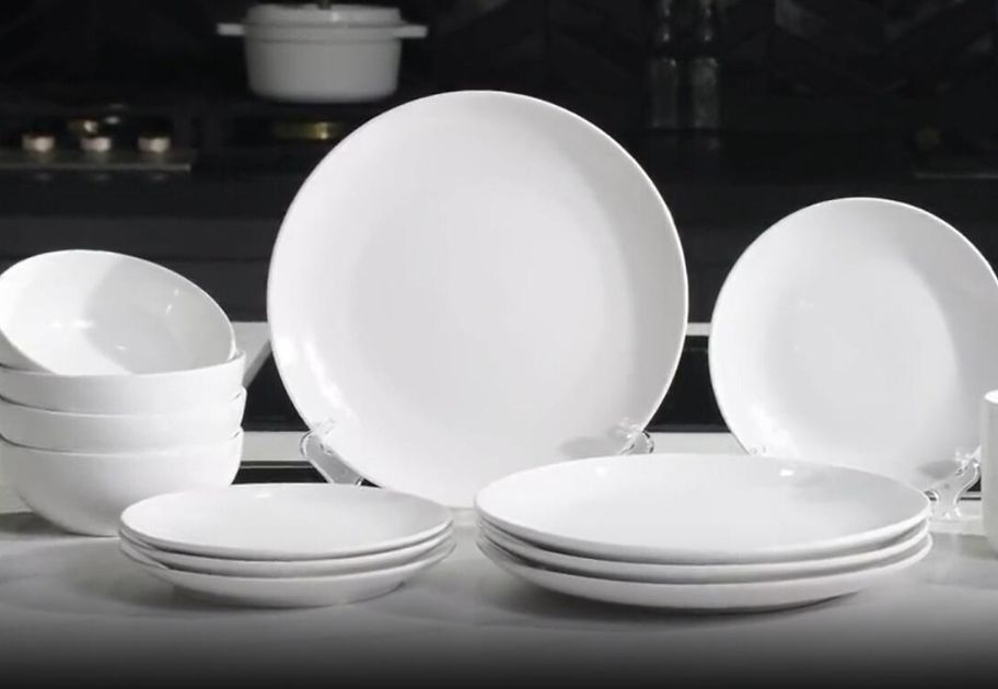 set of 12 glazed white dinnerware pieces on a kitchen counter with a stove in the background