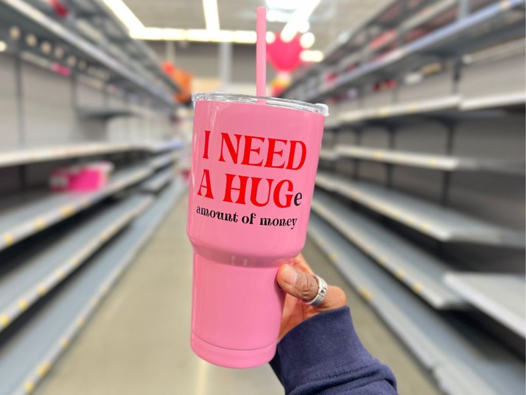 pink Valentine's Day tumbler that says I need a Hug(e) amount of money in women's hand