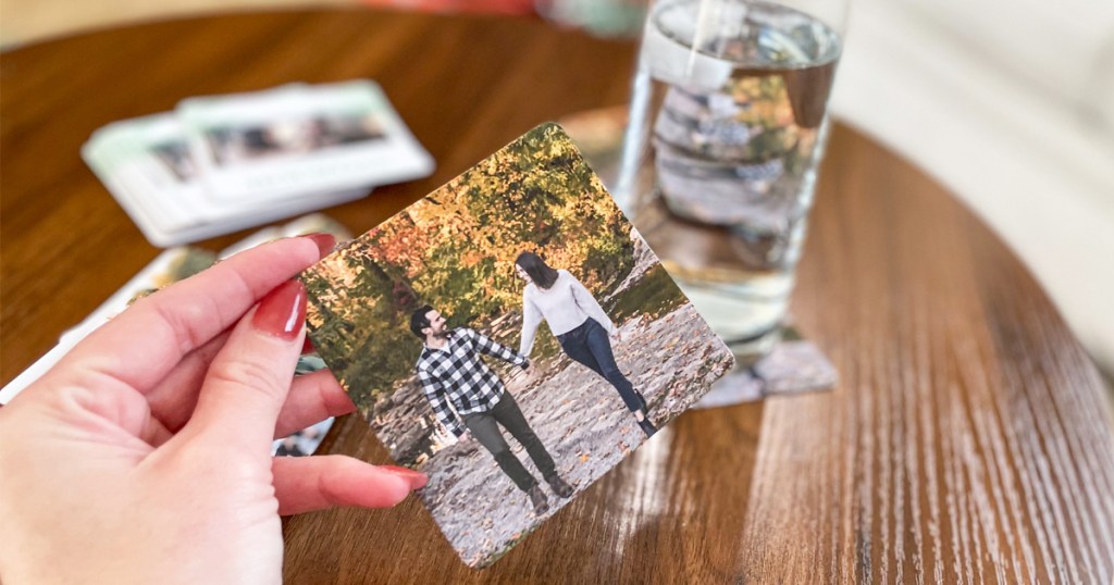 hand holding up a photo coaster with glass of water in background