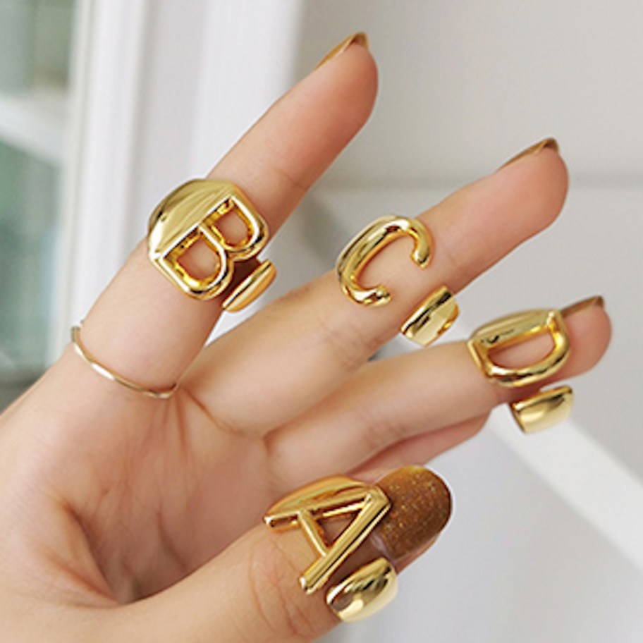 hand holding gold initial rings 