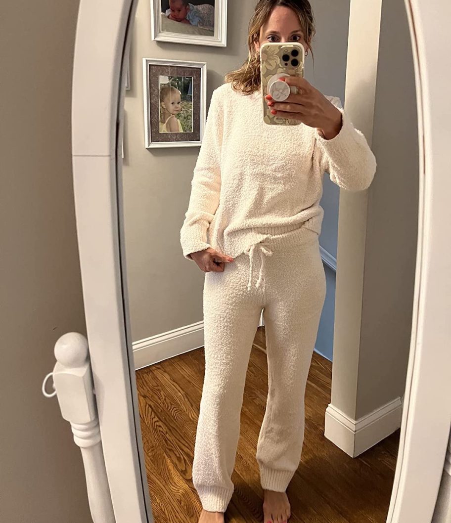 woman holding phone taking selfie in mirror wearing white loungewear set