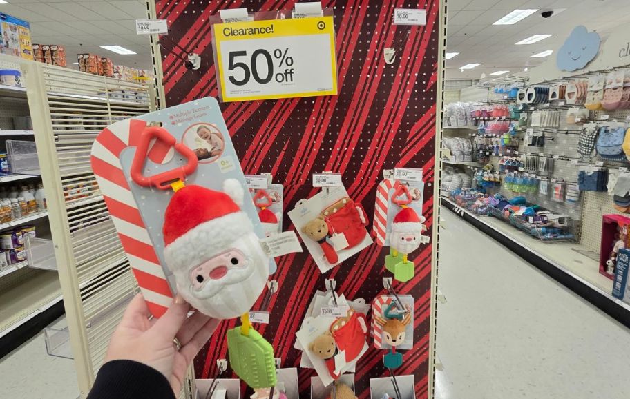 a womans hand holding a holiday baby toy infront of toy on a store shelf 