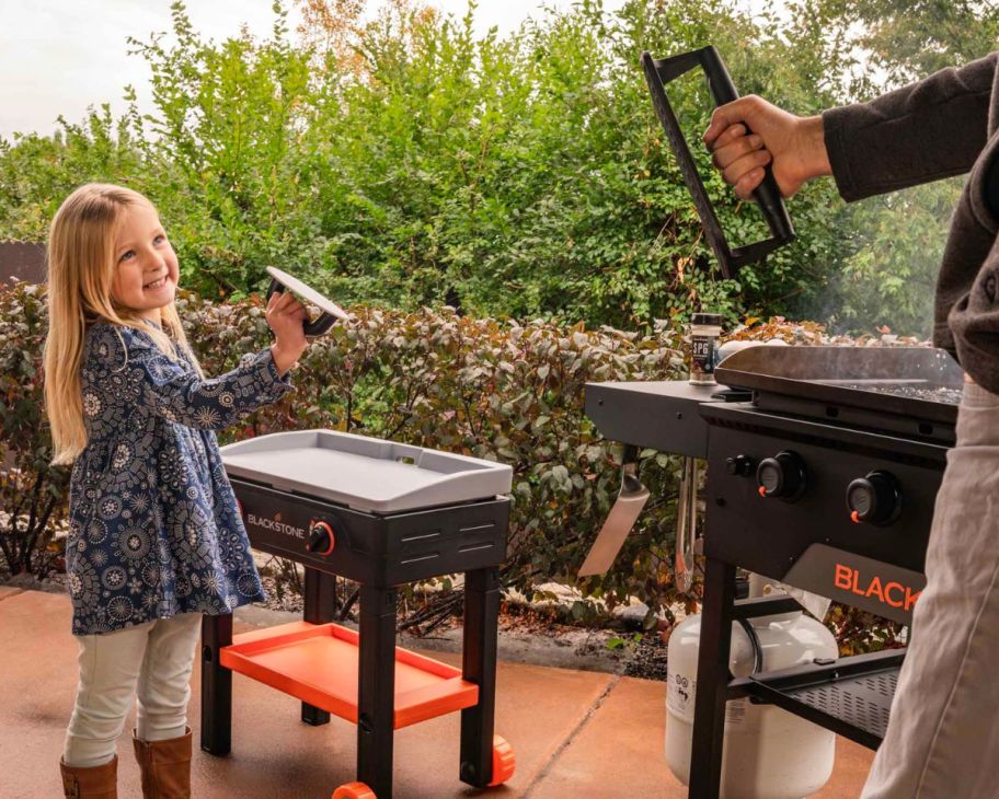 a little girl with a blackstone mini griddle and her dad with a full size version cooking on the patio