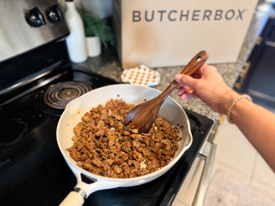 person cooking beef in a pan with a butcherbox package behind it