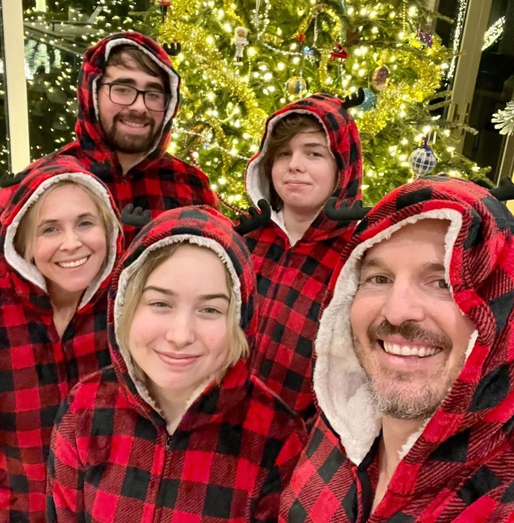 family wearing matching red and black plaid hoodie pajamas in front of christmas tree