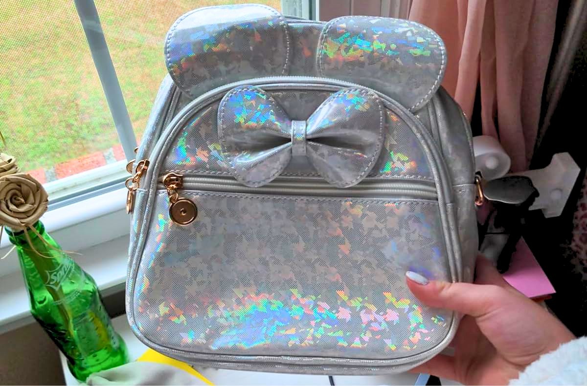 a womans hand holding a disney inspired mini backpack in silver