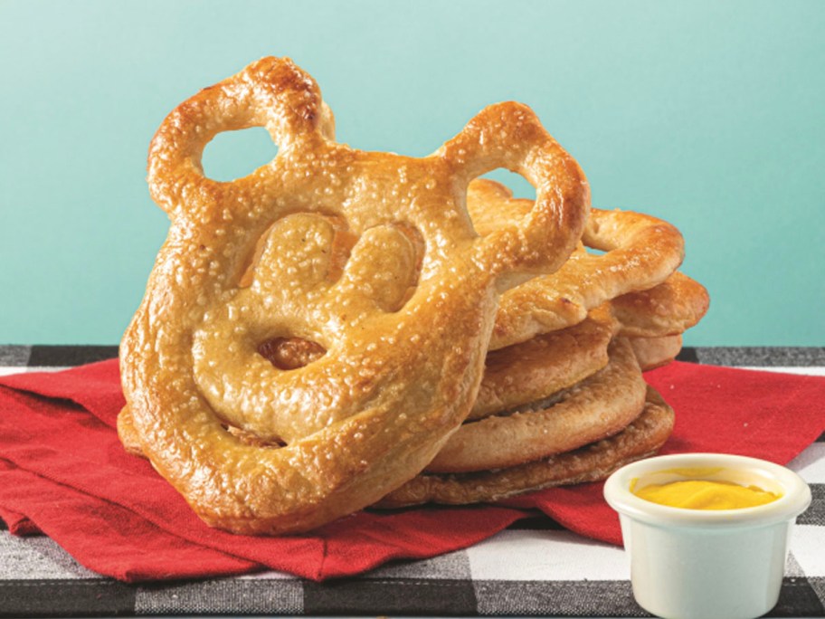 mickey mouse shaped pretzels stacked next to cup of mustard
