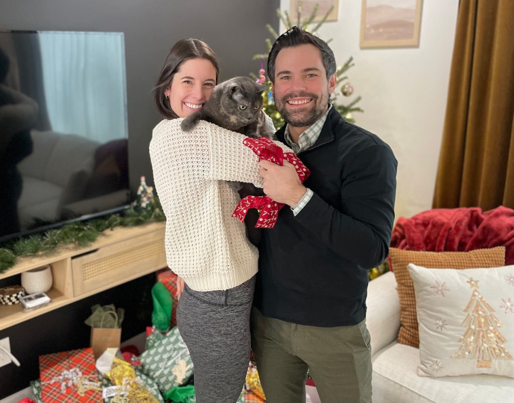 woman and man holding cat in front of christmas tree
